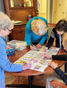 Four Tamarisk Senior Living Memory Care residents decorate a welcome sign on a table to greet a new neighbor