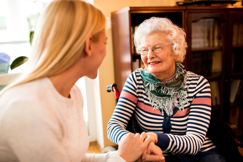 At Tamarisk Senior Living we are here to hold your hands all the way through the process of dementia and care. In this image a senior woman smiles while holding the hand of a younger woman.